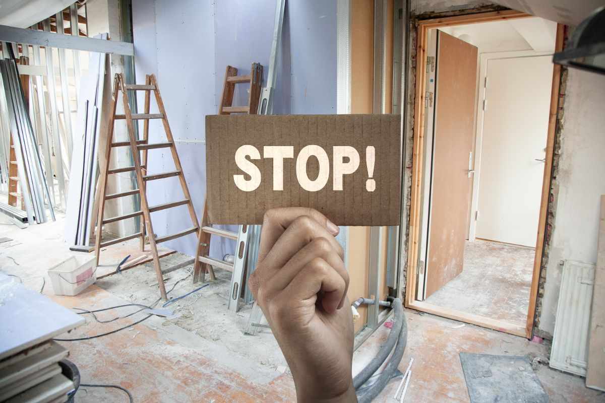 bagno in ristrutturazione e man che mantiene cartello con scritta stop
