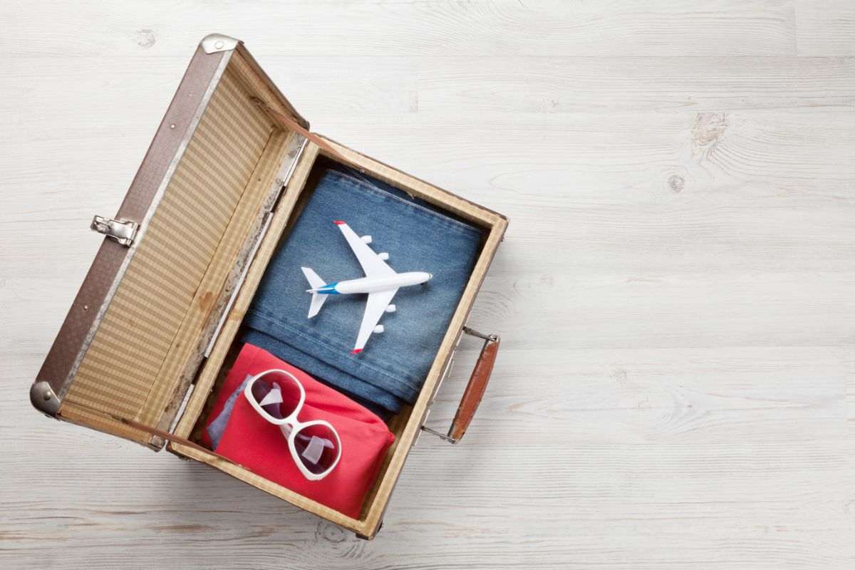 valigia con occhiali vestiti e modellino di aereo