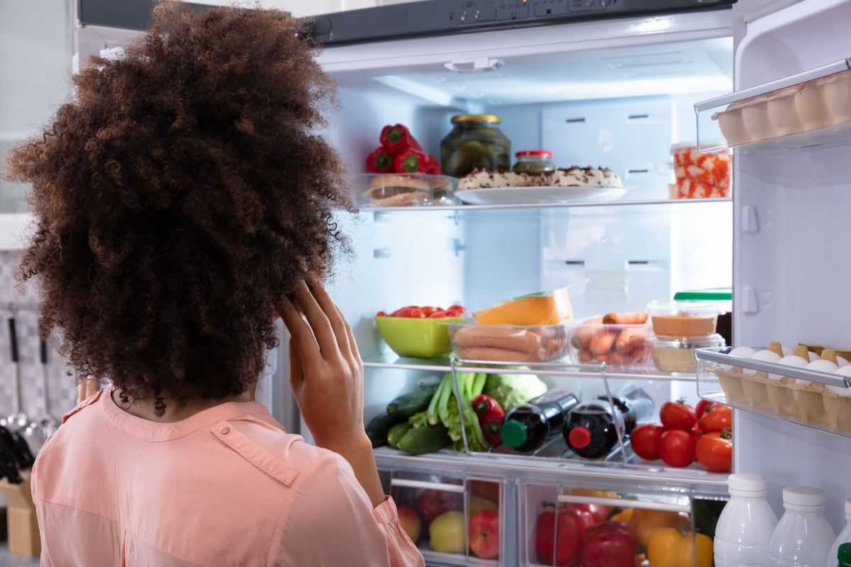 donna che guarda in un frigo aperto e pieno di cibo